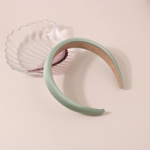 Détail d'un serre-tête en satin rembourré vert menthe sur un fond beige minimaliste