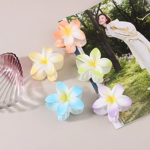 Détail de cinq pinces à cheveux en forme de fleur de frangipanier sur table beige