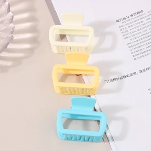 Close-up of three matte square hair claw clips in yellow and blue on a table