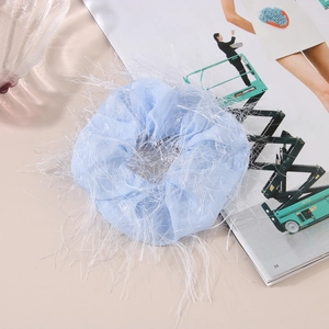 Close-up of a light blue mesh hair scrunchie with fringe detail on a fashion magazine