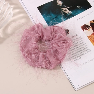 Close-up of pink mesh scrunchie with feather-like fringe details on a soft background