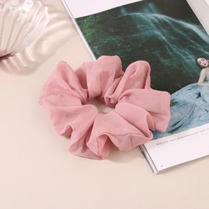 Grand chouchou élégant en mousseline rose avec design plissé sur une table épurée
