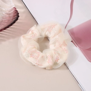 Détail du chouchou en tulle crème avec motif floral rose et texture élastique plissée