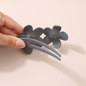 Detail view of a matte dark grey resin flower hair clip with a sturdy double floral design