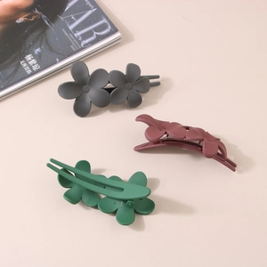 Three matte flower hair clips in dark grey, purple, and green on a fashion magazine