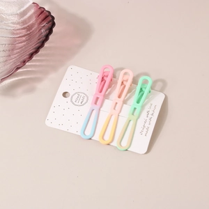 Gros plan de trois pinces à cheveux en métal dégradé macaron sur une carte blanche