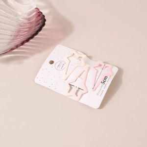 Star-shaped matte metal hair clips in soft cream and pink tones on a display card