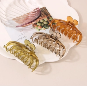 Three large transparent acrylic hair claws in amber, gray, and green on a white tray
