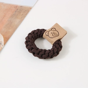 Détail d'un élastique à cheveux tressé marron avec un patch motif d'ours en cuir souple
