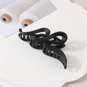 Détail d'une grande pince à cheveux noir mat avec design ondulé sur un plateau blanc