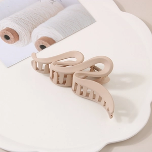 Détail d'une pince à cheveux mate beige au design ondulé sur un plateau de présentation