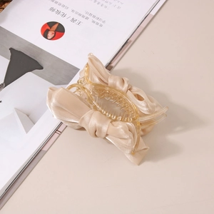 Détail d'une pince à cheveux avec nœud en satin champagne posée sur un magazine