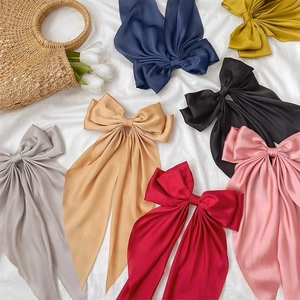 Flat lay of satin bow hair clips in various colors with long ribbons on white fabric