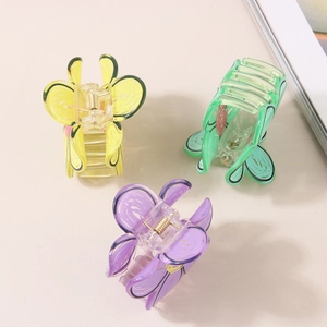 Three colorful butterfly hair clips in yellow, green and purple on a beige background