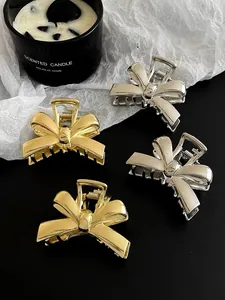 Polished gold and silver alloy bow hair claws displayed on a minimalist background