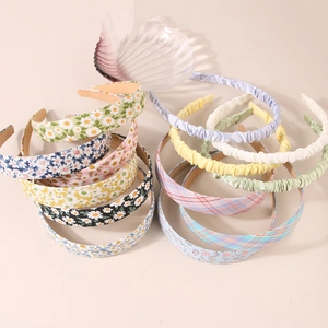 Detail of floral, pleated, and checkered fabric headbands on a minimalist beige surface
