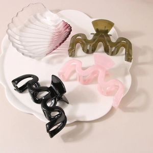 Three wave-shaped hair claws in black, pink, and green on a white ceramic petal tray