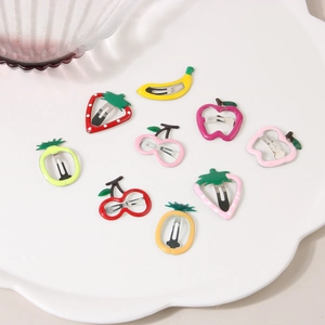 Detailed view of nine colorful fruit-shaped metal hair clips in a decorative white tray