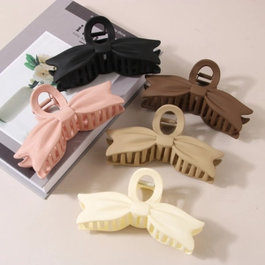 Dettaglio di cinque fermagli a fiocco opachi in nero, rosa, marrone, kaki e bianco crema