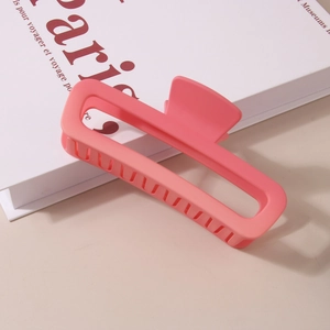 Matte coral pink rectangular hollow hair claw clip for women on a Paris book background
