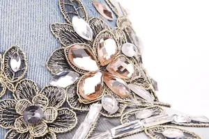 Macro shot of rhinestones and gold floral embroidery on light blue denim baseball cap