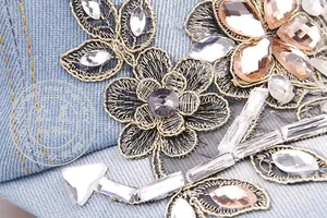 Detailed macro view of gold thread floral embroidery and colorful rhinestones on denim