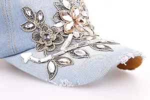Close-up of floral embroidery and sparkling rhinestones on light blue denim baseball cap