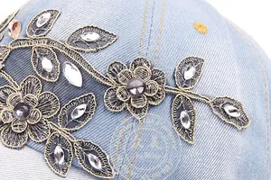 Close-up of golden floral embroidery and sparkling rhinestones on light blue denim cap