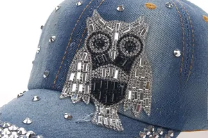 Close-up of rhinestone owl motif and rivet details on the blue denim baseball cap