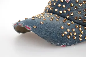 Détail de la casquette en jean avec strass ambrés et bordure de visière effilochée