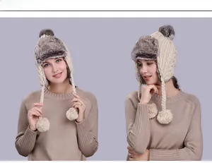 Detail view of beige cable knit trapper hat with grey faux fur lining and pompom ties