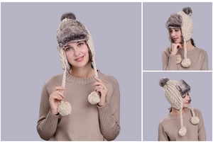 Close-up of cable knit winter trapper hat with gray faux fur trim and fluffy pom-poms