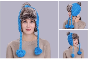 Close-up of blue cable knit trapper hat with grey faux fur lining and large pom-poms