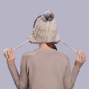 Back view of beige cable-knit trapper hat with grey faux fur pompom and plush lining