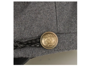 Macro detail of bronze crest button and black braided cord on dark grey wool newsboy cap