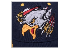 Macro close-up showing detailed eagle embroidery on blue cotton twill baseball cap