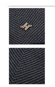 Macro view of high-density navy knit fabric featuring a vintage bronze metal H badge