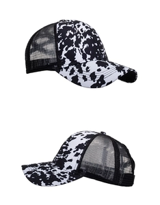 Detail view showing black and white cow print fabric with black breathable mesh on trucker hat