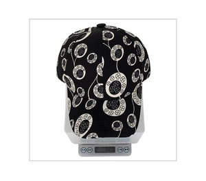 Detail view of a black baseball cap with clover print weighing 72.0g on a digital scale