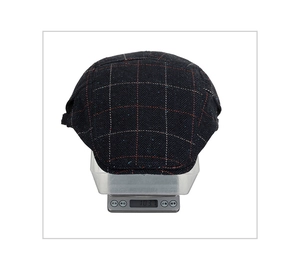 Detailed view of winter herringbone plaid beret cap being weighed on an electronic scale