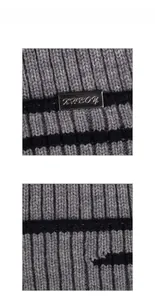 Détail d'un bonnet en maille grise avec rayures noires et plaque logo en métal
