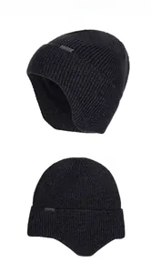 Detail of black thick knit beanie with warm ear flaps and small metal logo tag