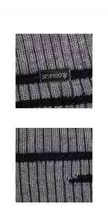 Close-up of grey ribbed knit texture with black stripes and silver metal logo plate