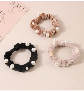 Detail of three velvet scrunchies with white pearls in black, brown and pink colors