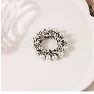Detail of tweed hair scrunchie with white pearls and gold thread on a ceramic tray