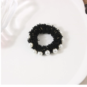 Detail of a black velvet scrunchie decorated with white pearls and gold thread accents