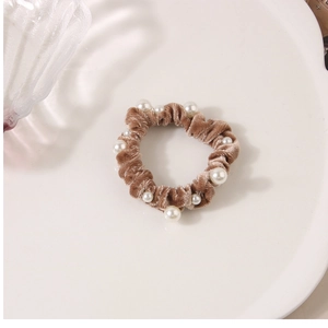 Macro detail of brown velvet scrunchie with white pearl accents on a white plate