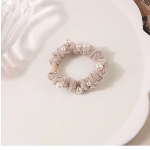 Macro detail of khaki velvet hair scrunchie with elegant pearls on a ceramic tray