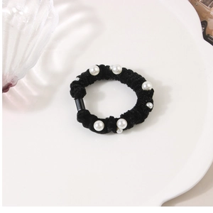 Close-up of black velvet scrunchie with white pearls on a minimalist white tray