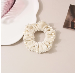 Dettaglio di scrunchie in velluto crema con perle bianche su un piatto di ceramica